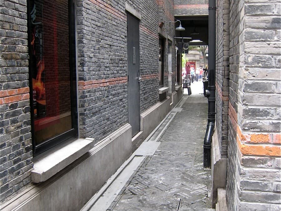 A shikumen lane in Shanghai's Xintiandi, with grey brick walls, arched doorways, and shops along the passage