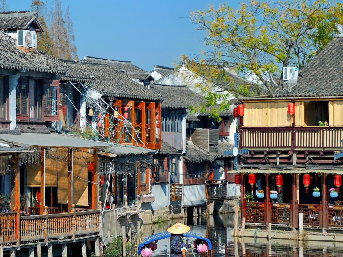 A water-town canal with covered boats, white-walled grey-tiled houses built right against the water