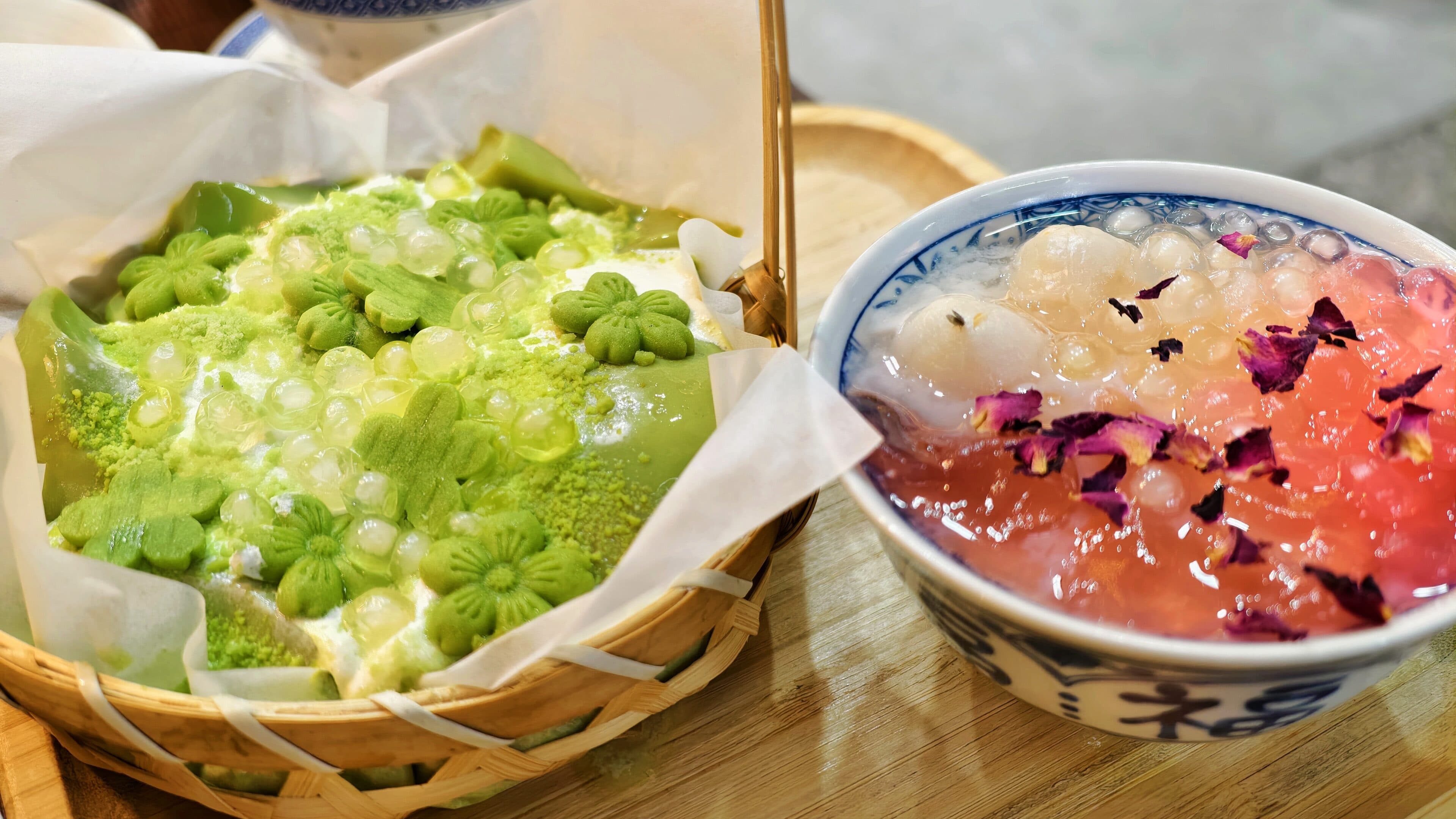 Two plates of dessert, green cake and pink syrup, with a bamboo basket and porcelain bowls