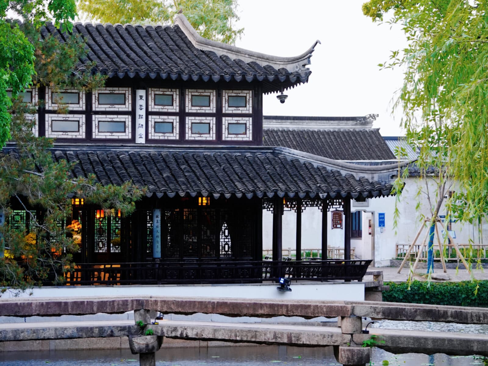 A waterside hall and zigzag bridge in a Suzhou garden, white walls and planting mirrored in the pond