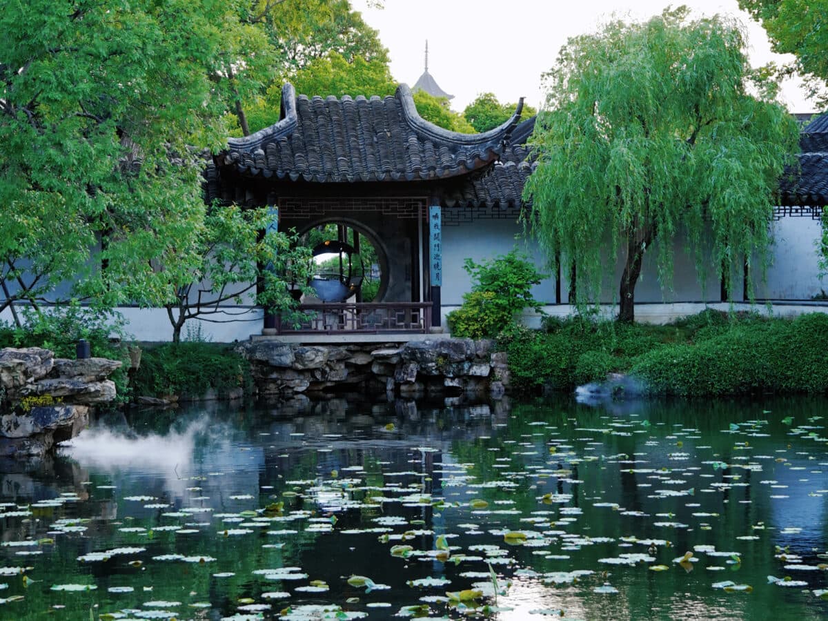 The lake in a Suzhou garden with a hall and willows on the far bank, the water still as a mirror