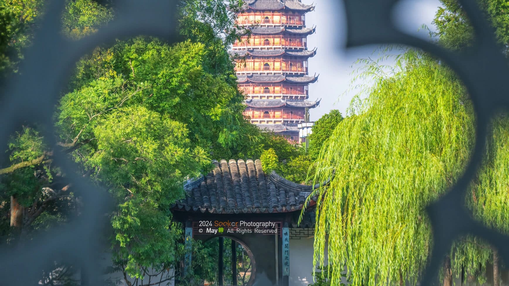 A multi-storey brick pagoda seen through a garden lattice window, a classic Suzhou framed view