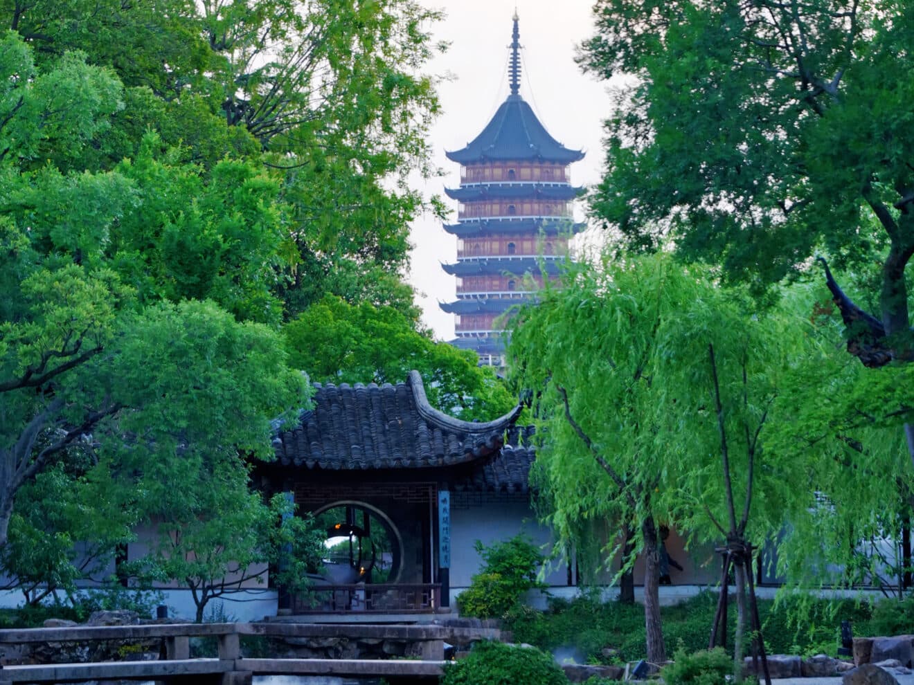A garden pond and zigzag bridge with willows and a pavilion, the Tiger Hill pagoda standing beyond