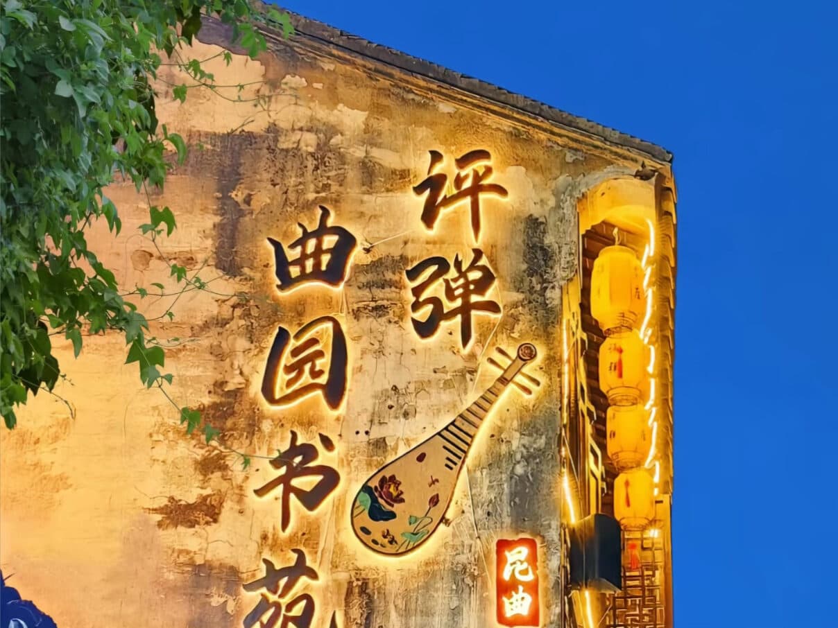 A lit signboard for a pingtan storytelling venue at night, with a pipa motif painted on the wall