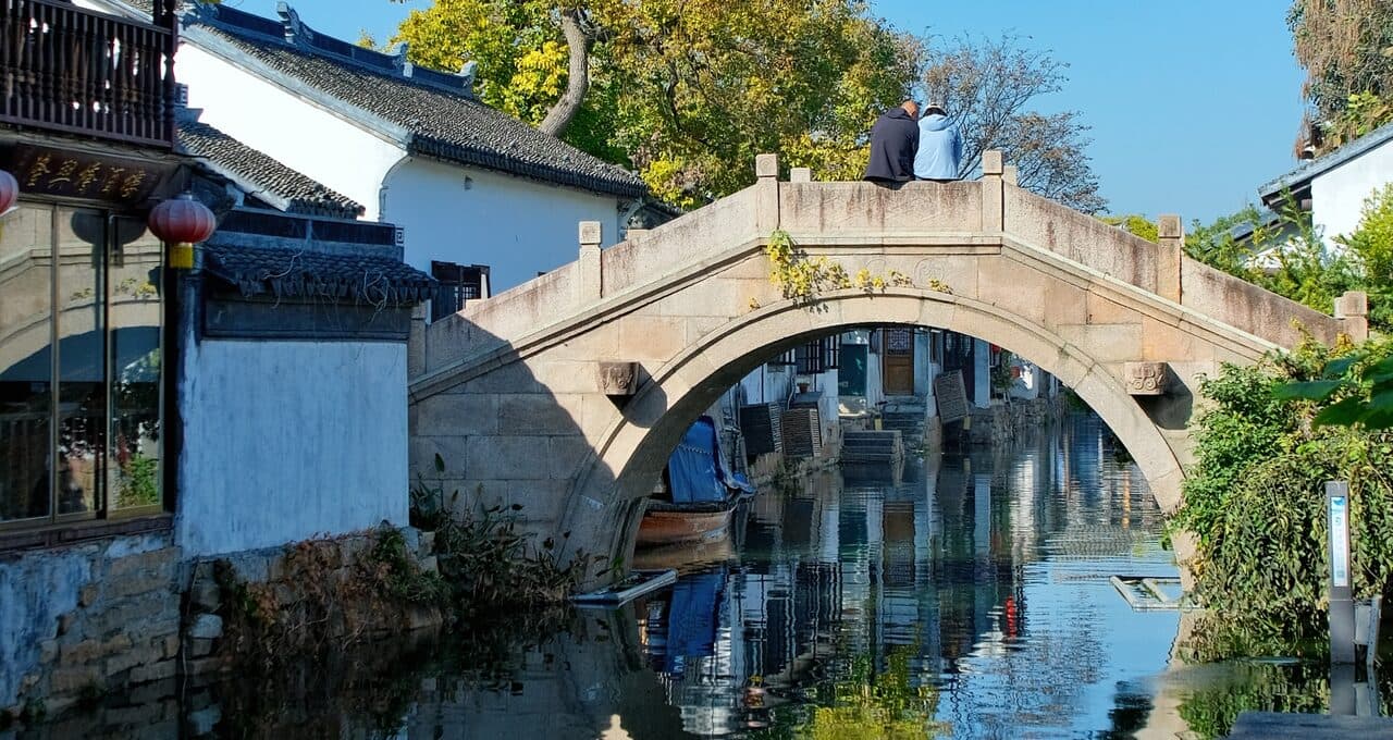 A stone arch bridge and canal near Hanshan Temple, the arch fully mirrored in the water between whitewashed houses