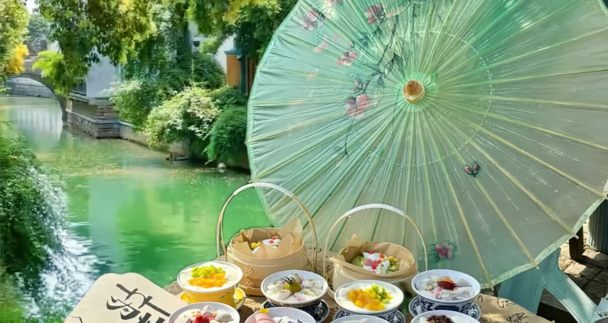 A Suzhou tea-snack table: a teapot and cups with small dishes of pastries beside an oil-paper umbrella