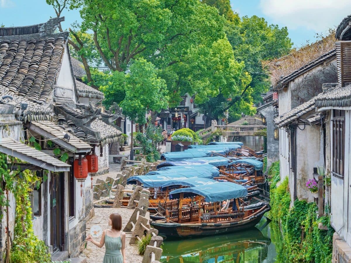 A water-town lane at dusk: red lanterns lit along the houses and wooden boats moored on the canal