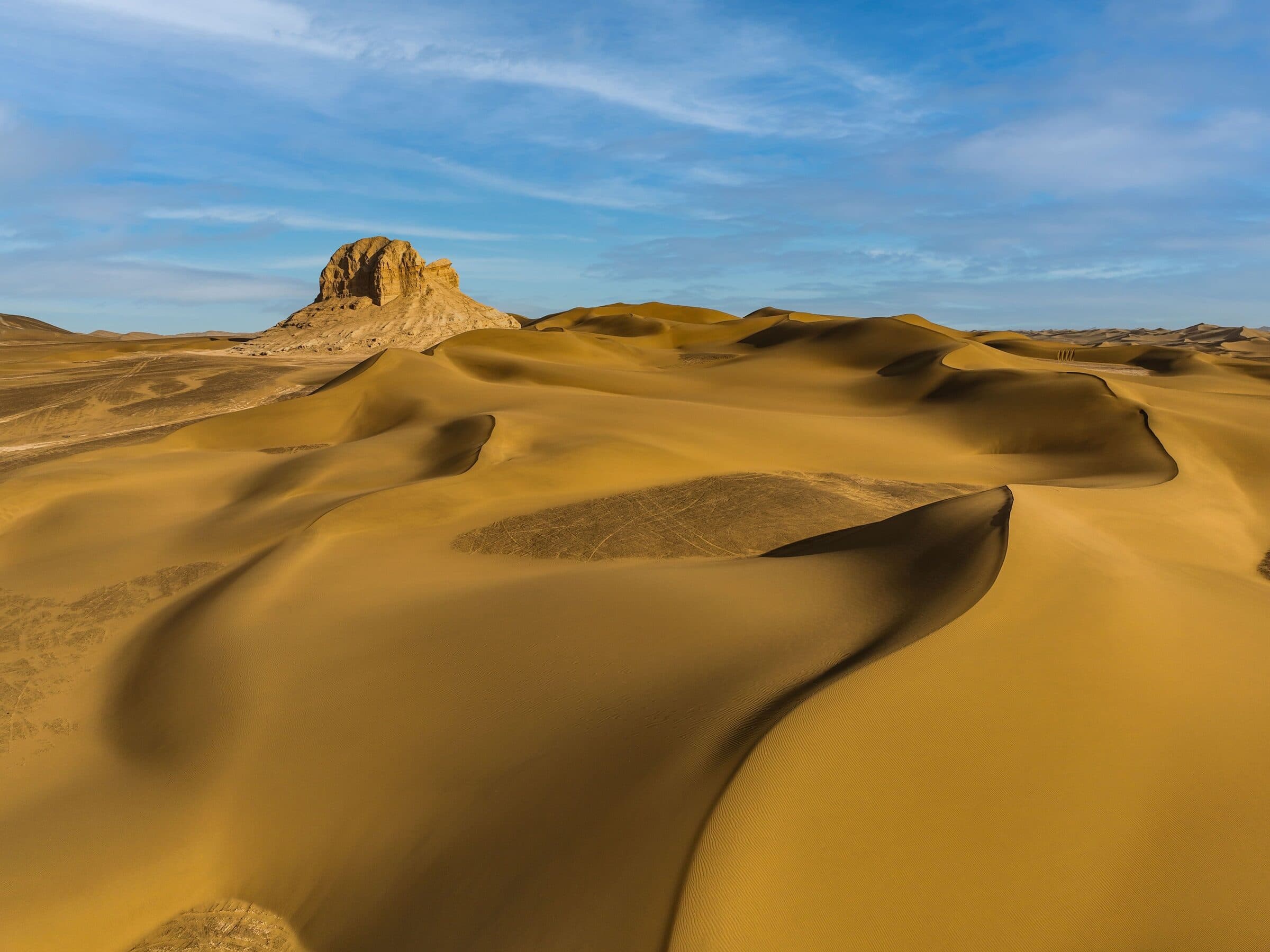 Golden dunes and an eroded rock outcrop in the Kumtag Desert
