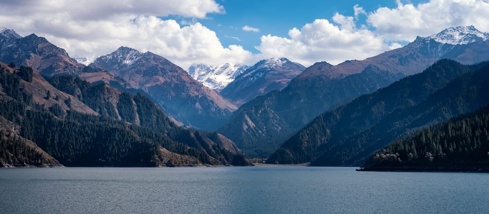 A Tianshan alpine lake with snow-dusted peaks and conifer slopes