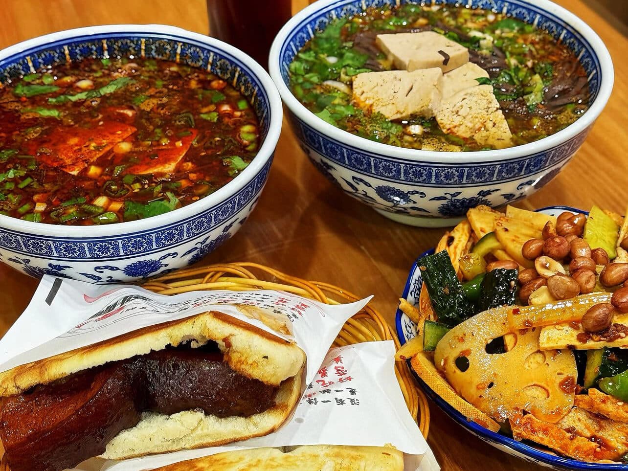 A Xi'an set meal on one table: two bowls of paomo, a plate of cold side dish and a filled roujiamo, with Ice Peak sodas