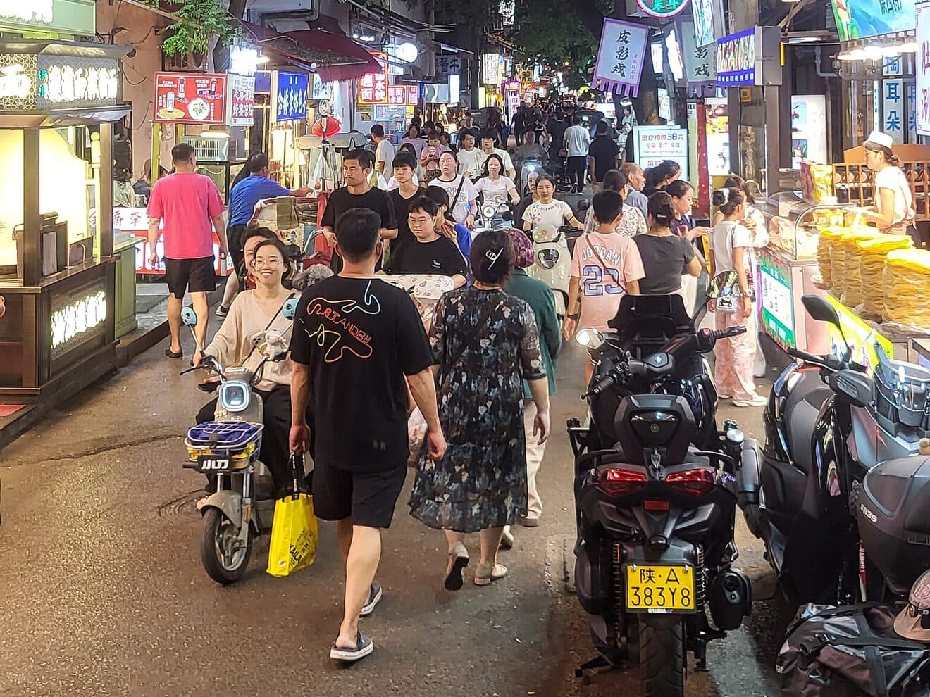 Xi'an's Sajinqiao Muslim Quarter at night, with lit food stalls, pavement, and passing diners