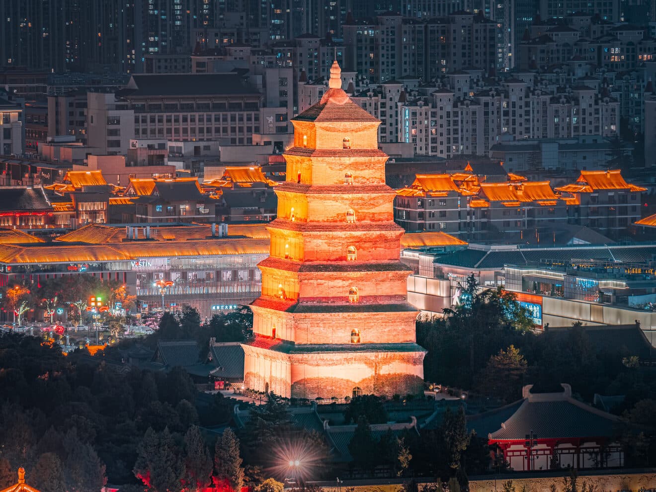 The Big Wild Goose Pagoda at night: the seven-storey brick pagoda is lit in warm light against the city's lit towers behind