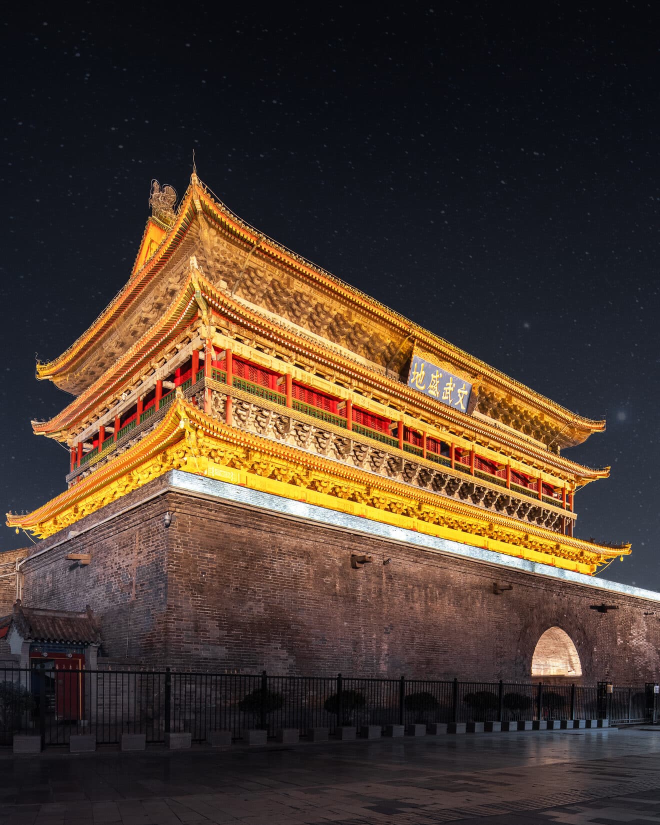 Xi'an's gate tower and brick city wall at night: warm lighting outlines the triple-eaved pavilion and battlements, with the moat-side walkway lit below