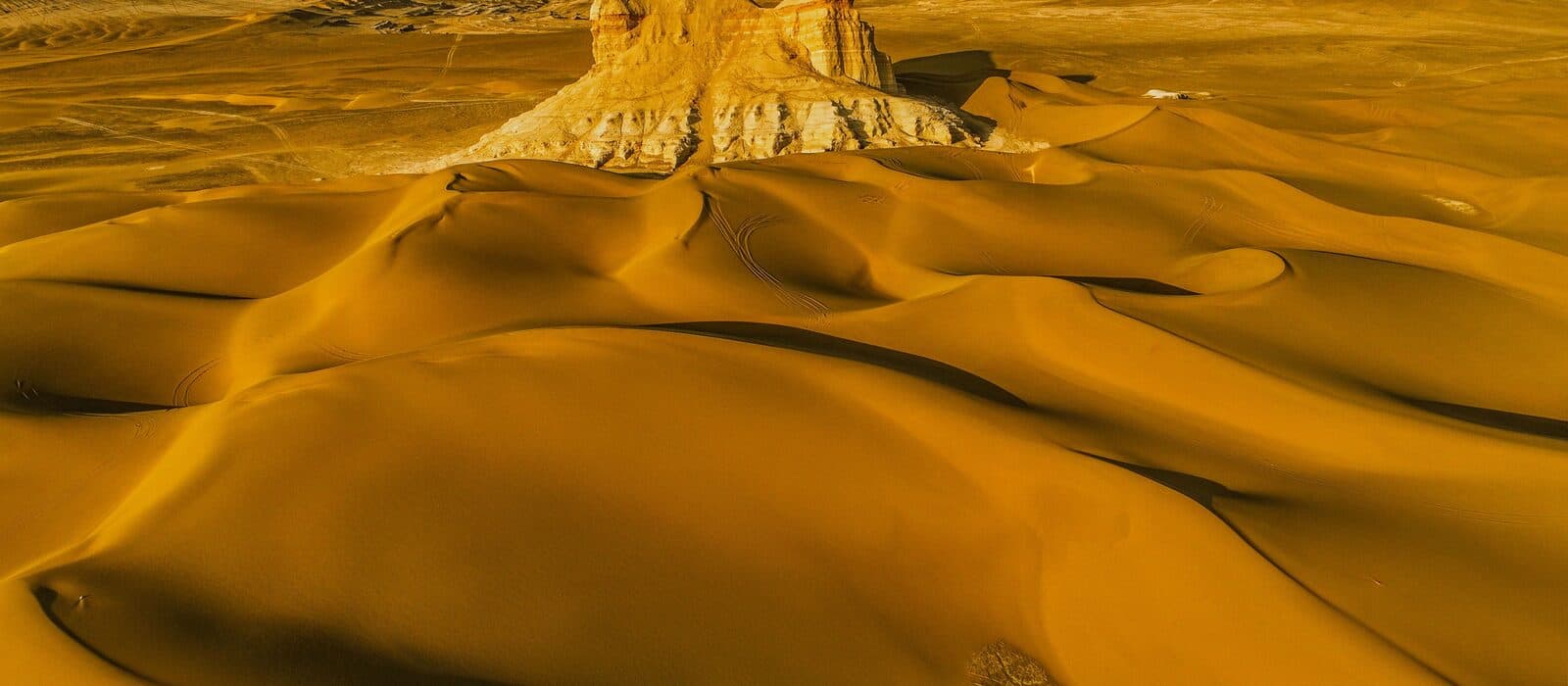 Golden dunes and an eroded rock outcrop in the Kumtag Desert