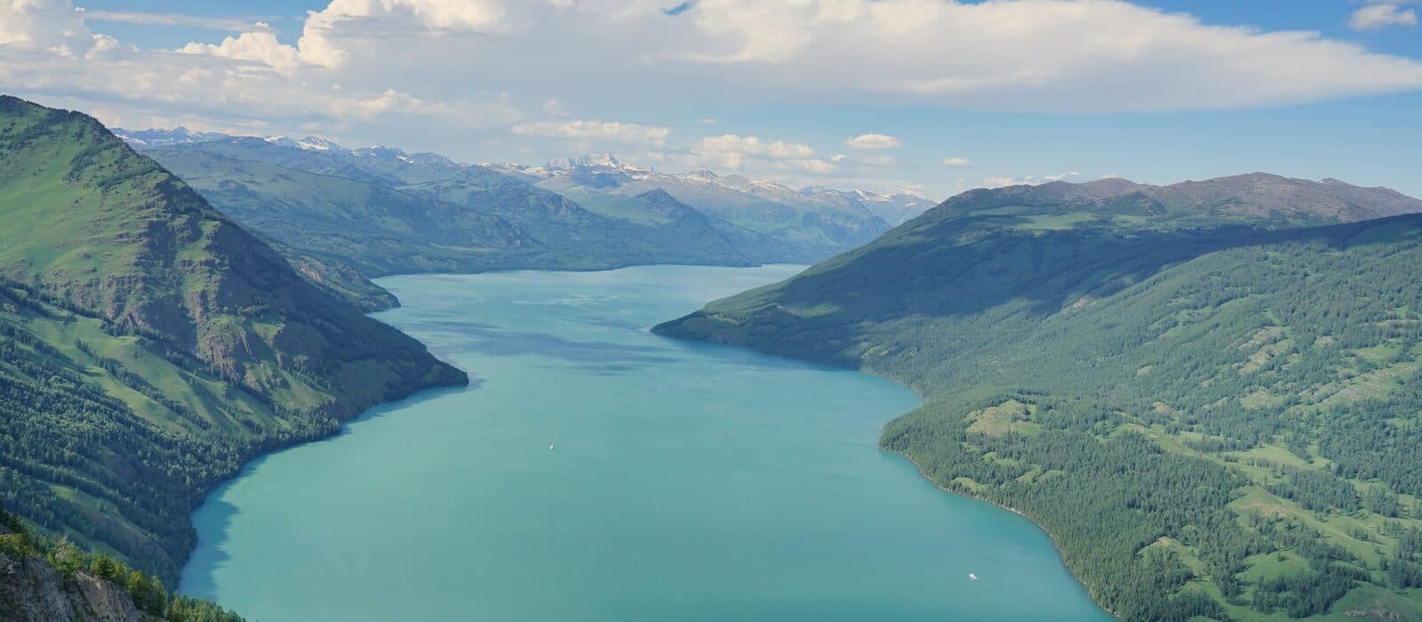 A turquoise lake winding between green forested ridges, seen from above
