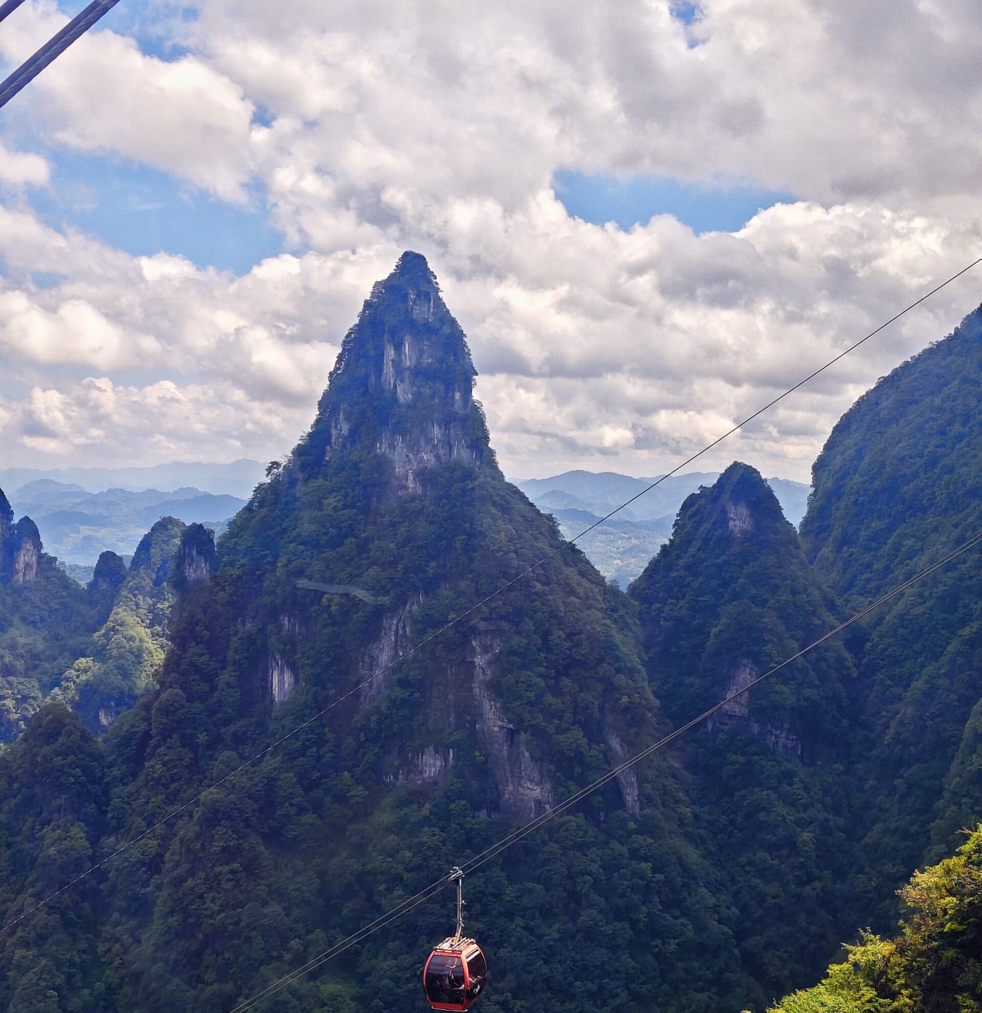 Red cable car cabin on the cableway above the forested peaks