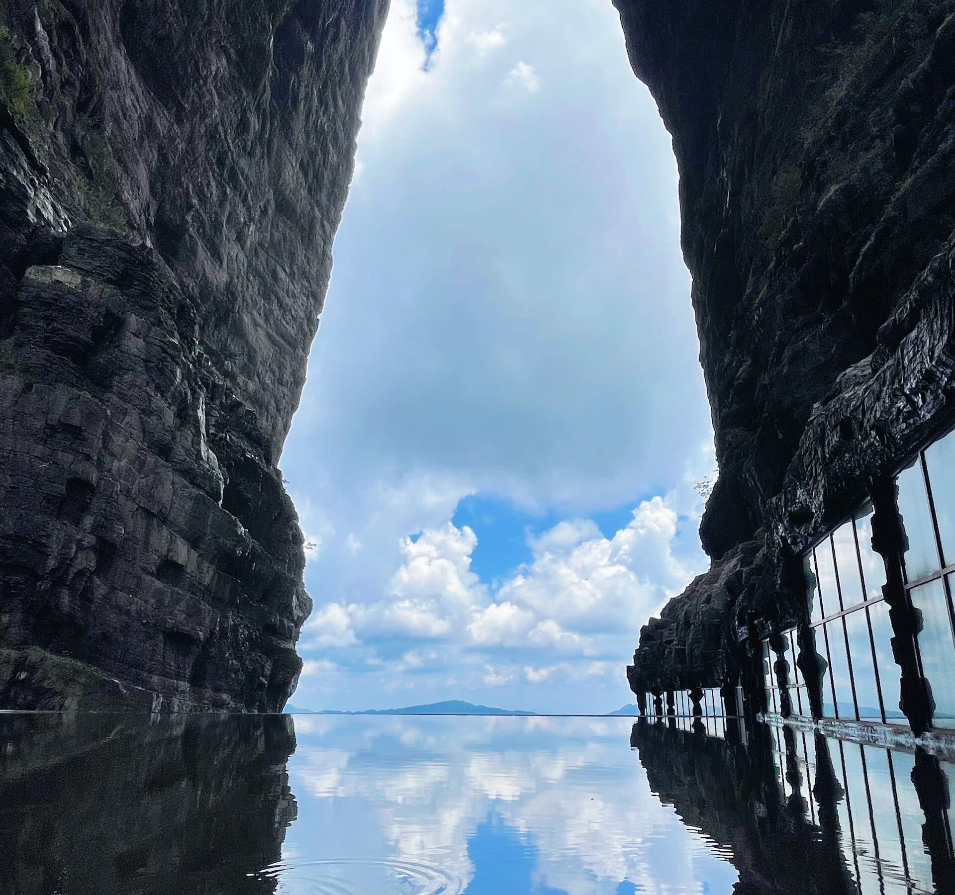 Still pool mirroring the dark cliff walls and their glass walkway