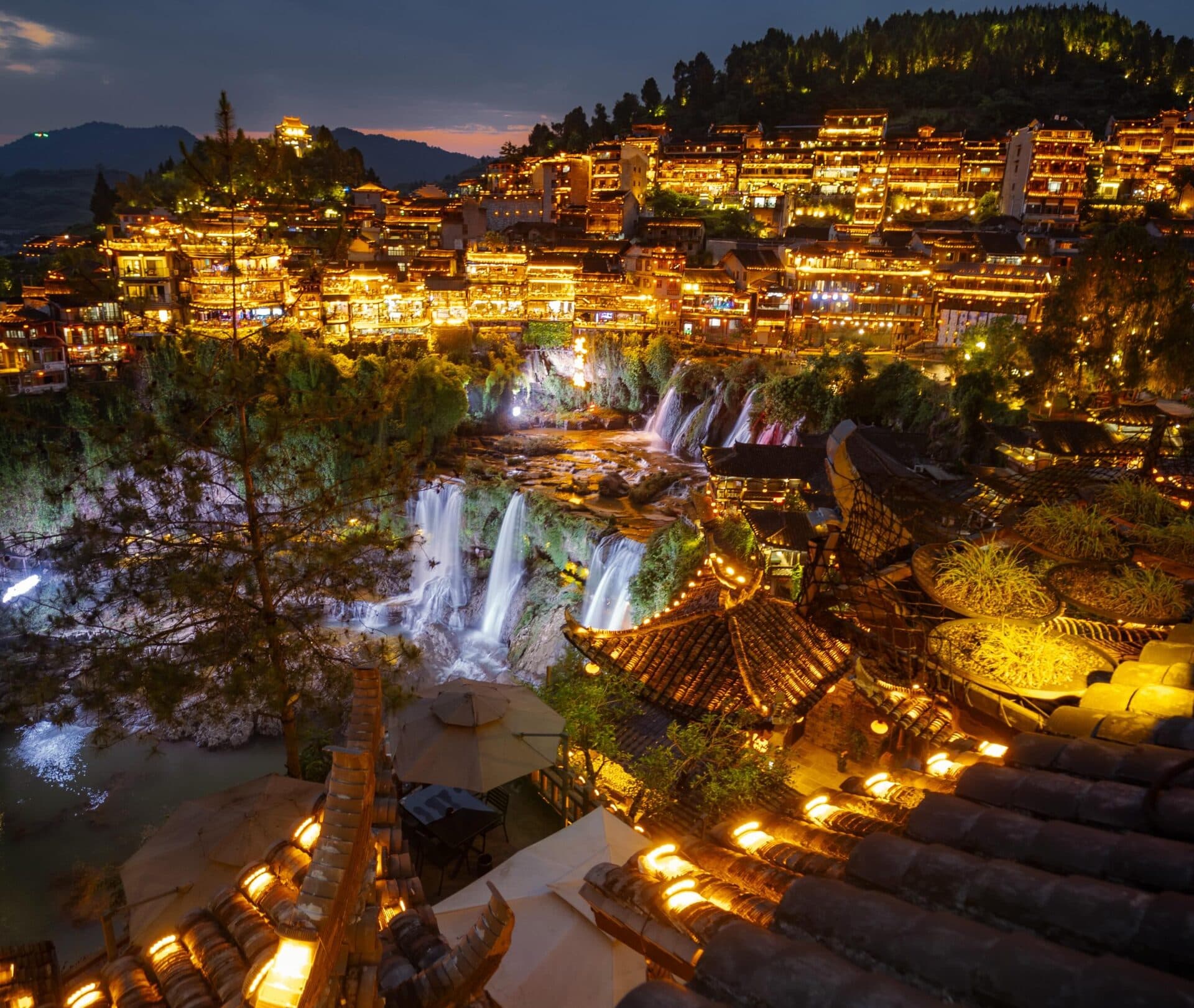 Night view over tiled roofs toward the lit old town