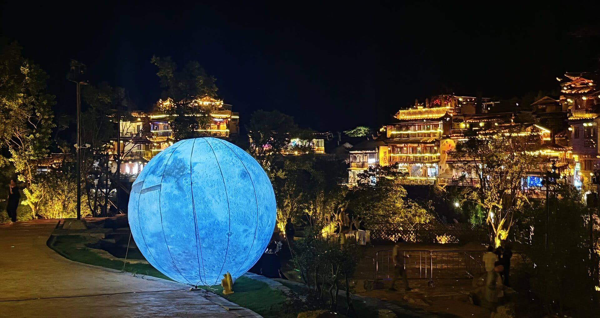 Glowing moon installation on a night path below the old town