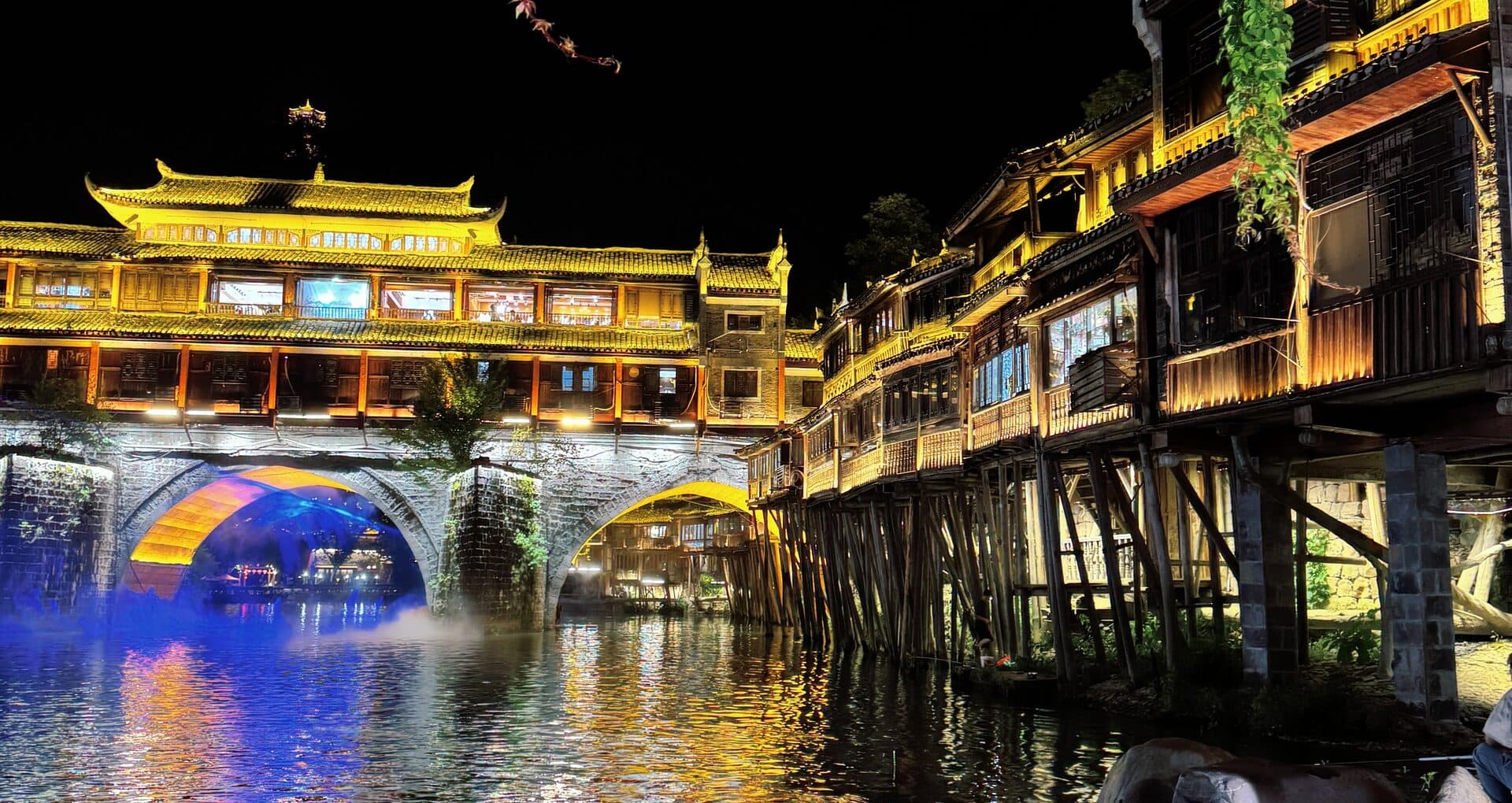 Night view of the old town bridge with stone piers and a willow