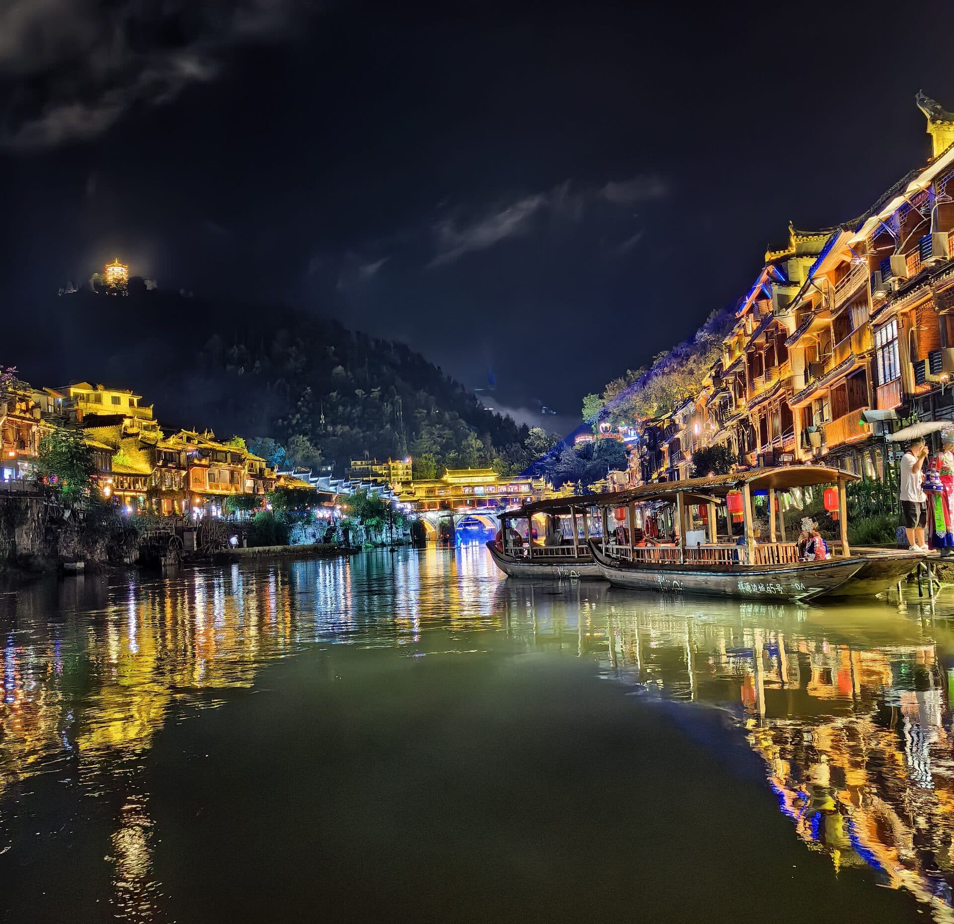 Night river with moored boats and lit houses along both banks