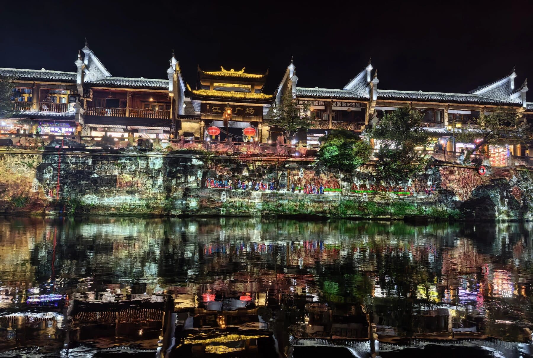 Night riverside town with lit buildings and boats on the water