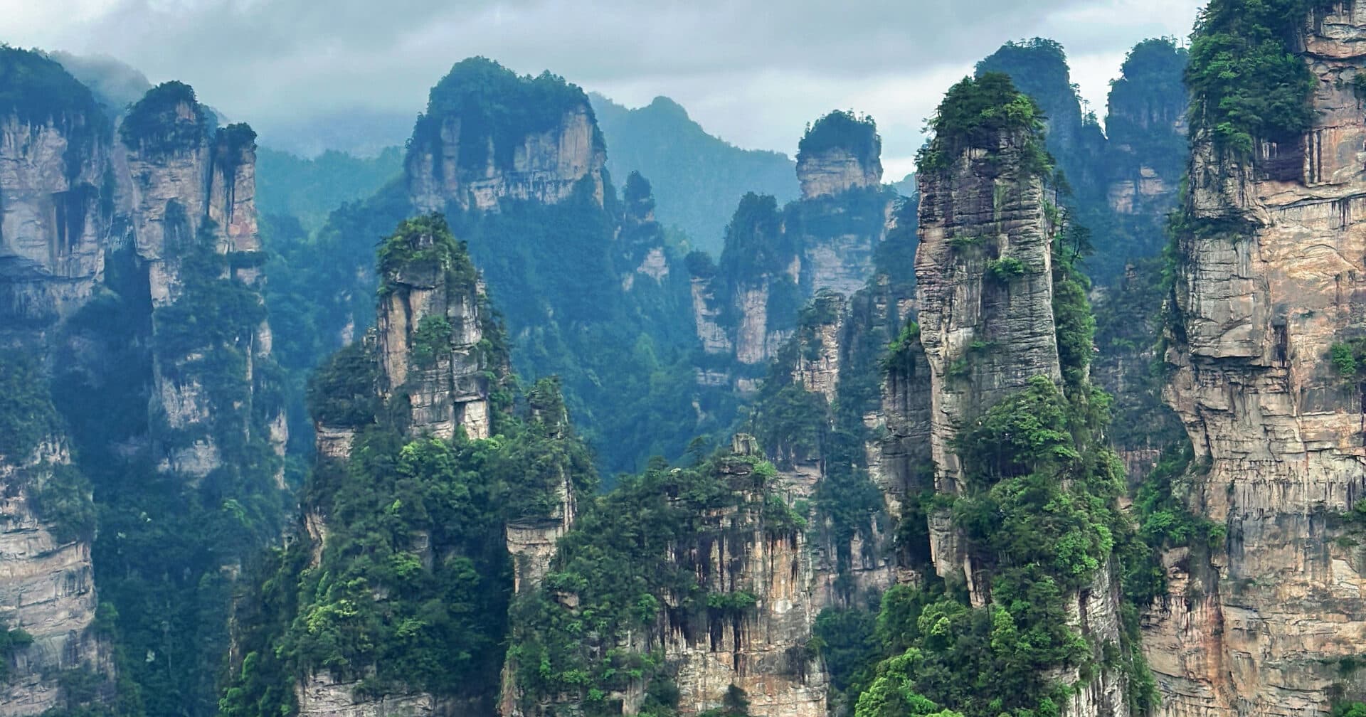 Sandstone pillars rising in layers above the forested valley under an overcast sky