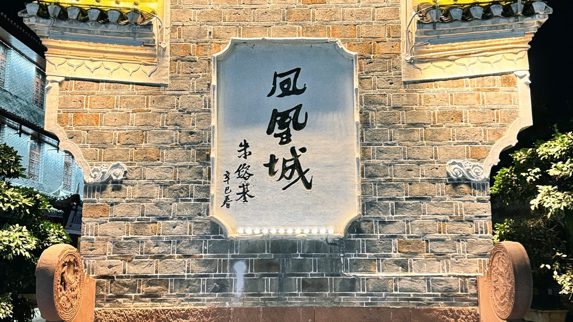 Warm-lit old-town brick wall at night with a carved stone plaque set into it
