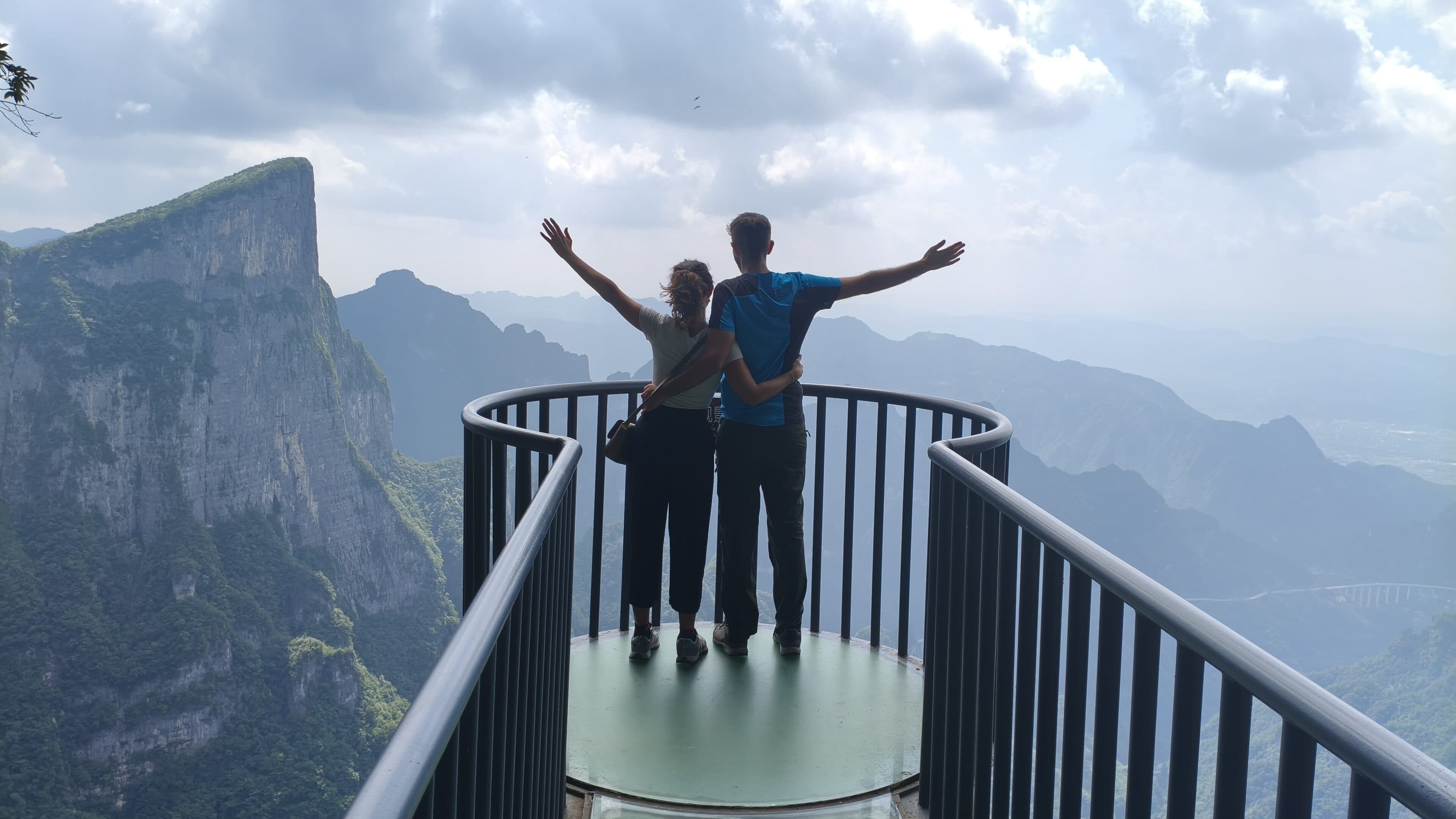 Two visitors on a circular glass-floored viewing platform above the cliffs