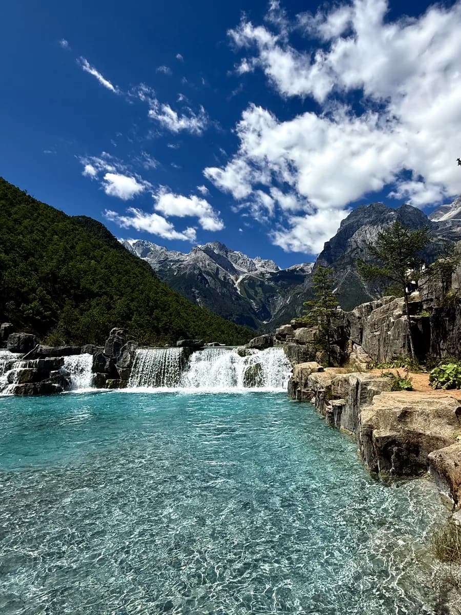 Turquoise terraced pools and a low waterfall at Blue Moon Valley, rocky banks and peaks beyond