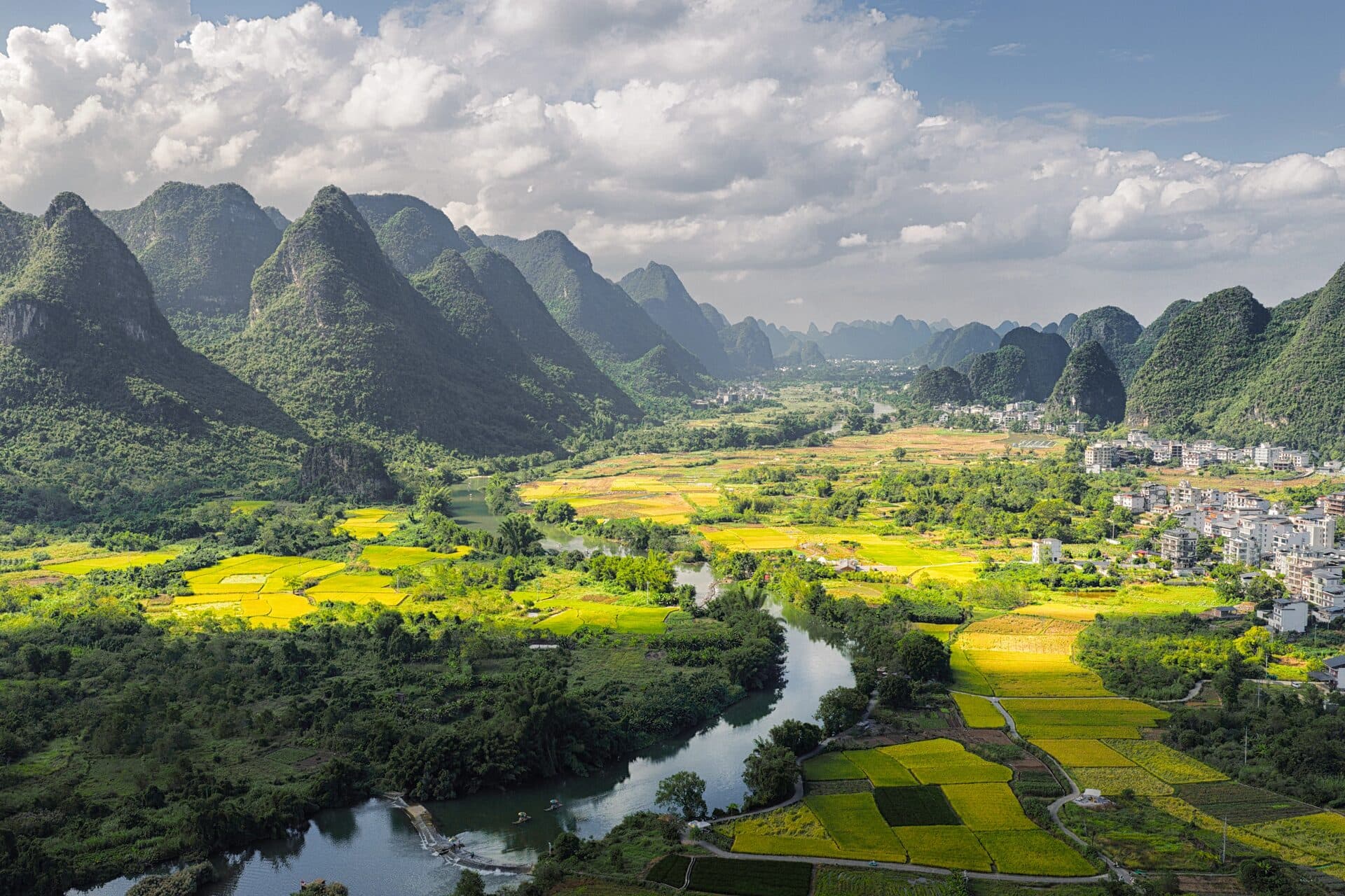 A river winding between karst peaks past yellow fields and a village