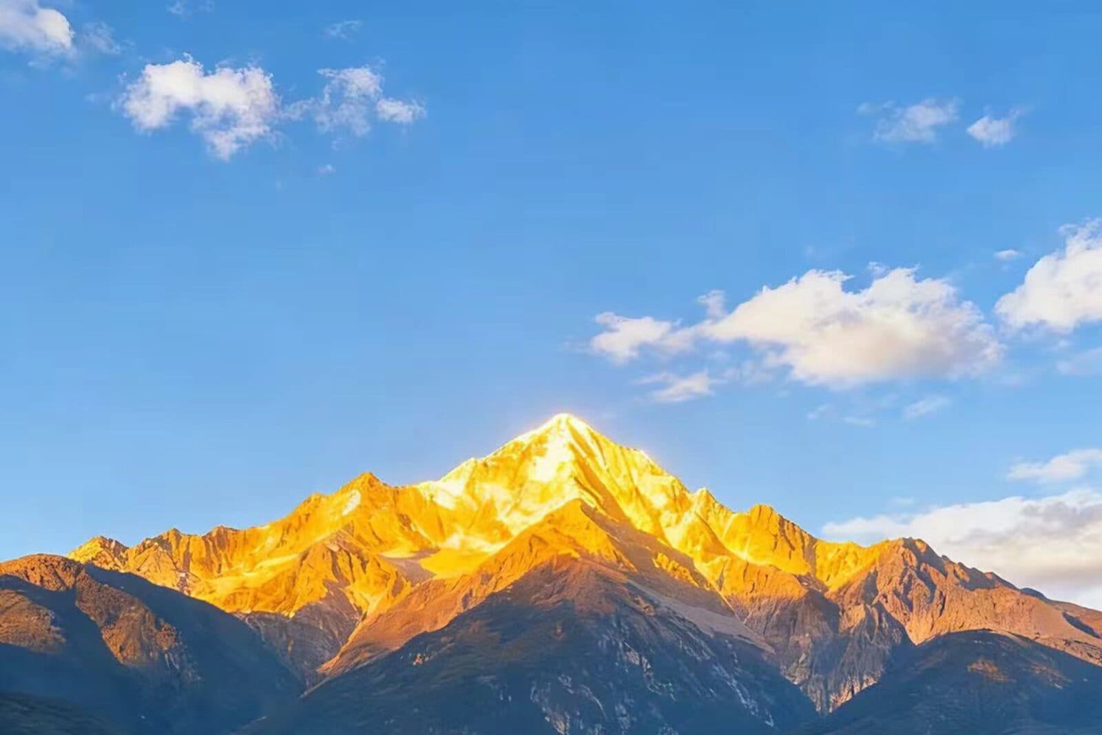 A snow mountain summit lit gold at sunrise under a blue sky with clouds